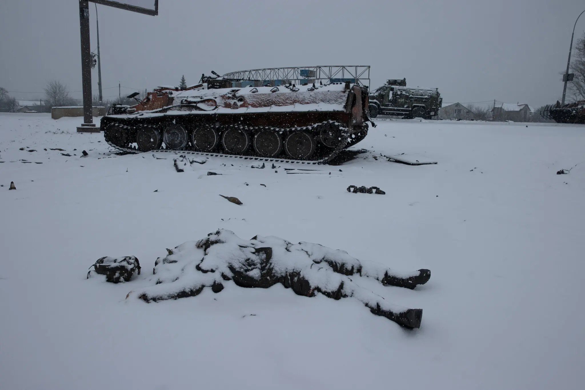 The corpse of a soldier covered in snow against the background of abandoned military equipment. Ukraine