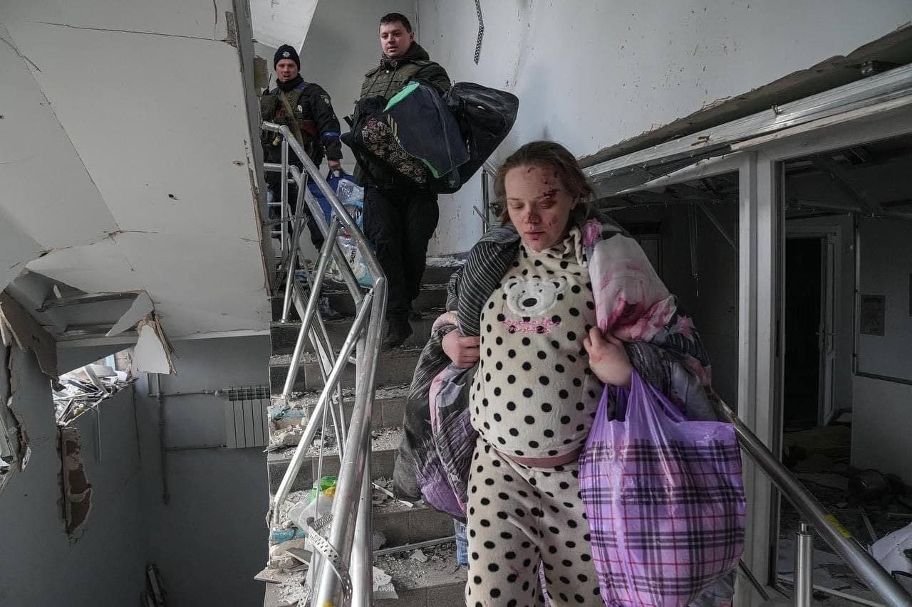 A pregnant woman descends the stairs from the destroyed maternity hospital