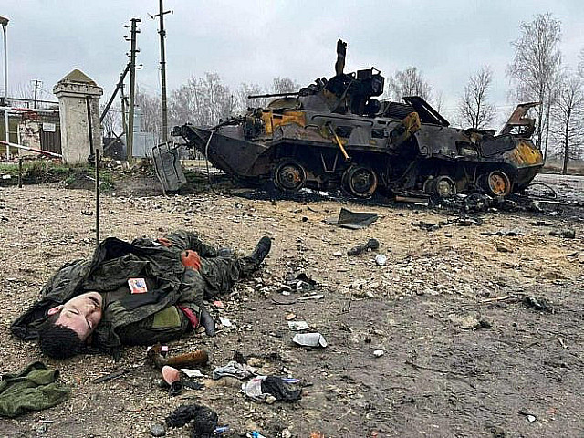 Труп российского воненного на фоне сгоревшего БТР